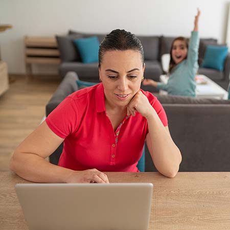 Foto van moeder achter laptop, dochter op de bank.